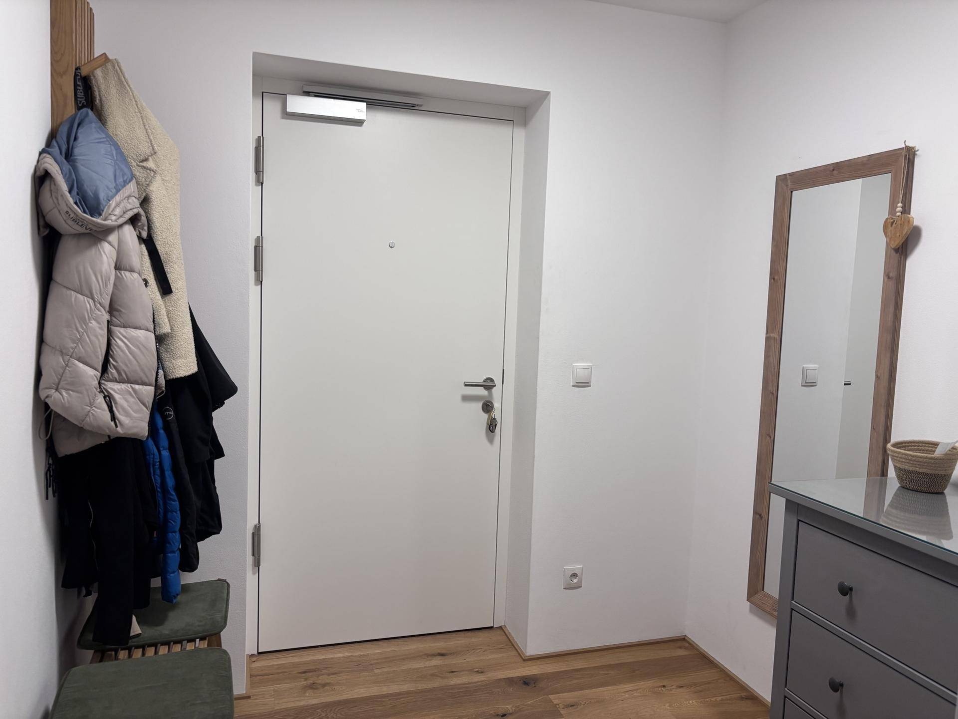 Eingangsbereich mit Garderobe, Holzboden und weißer Eingangstür.