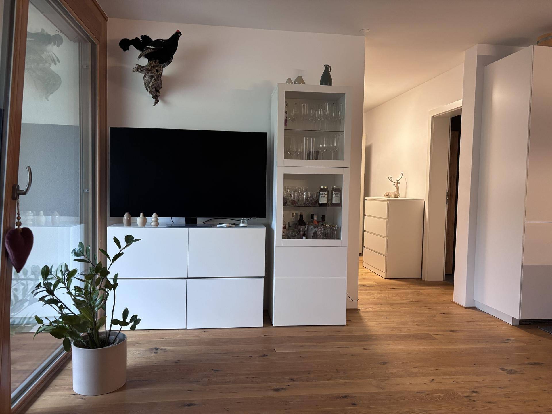Wohnbereich mit TV-Möbeln, Vitrine und Zugang zu weiteren Räumen.