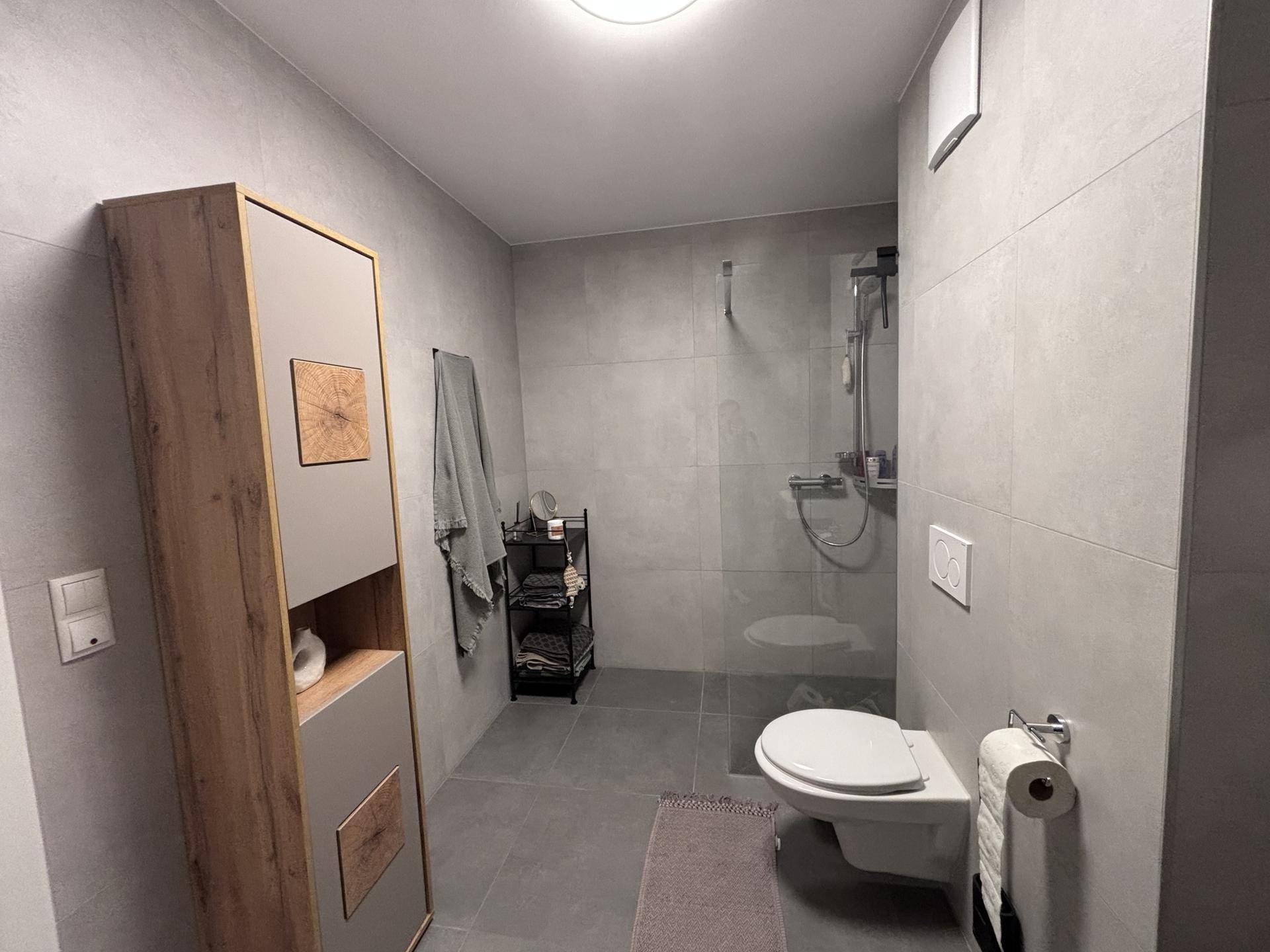 Modernes Badezimmer mit begehbarer Dusche, WC und grauen Fliesen.