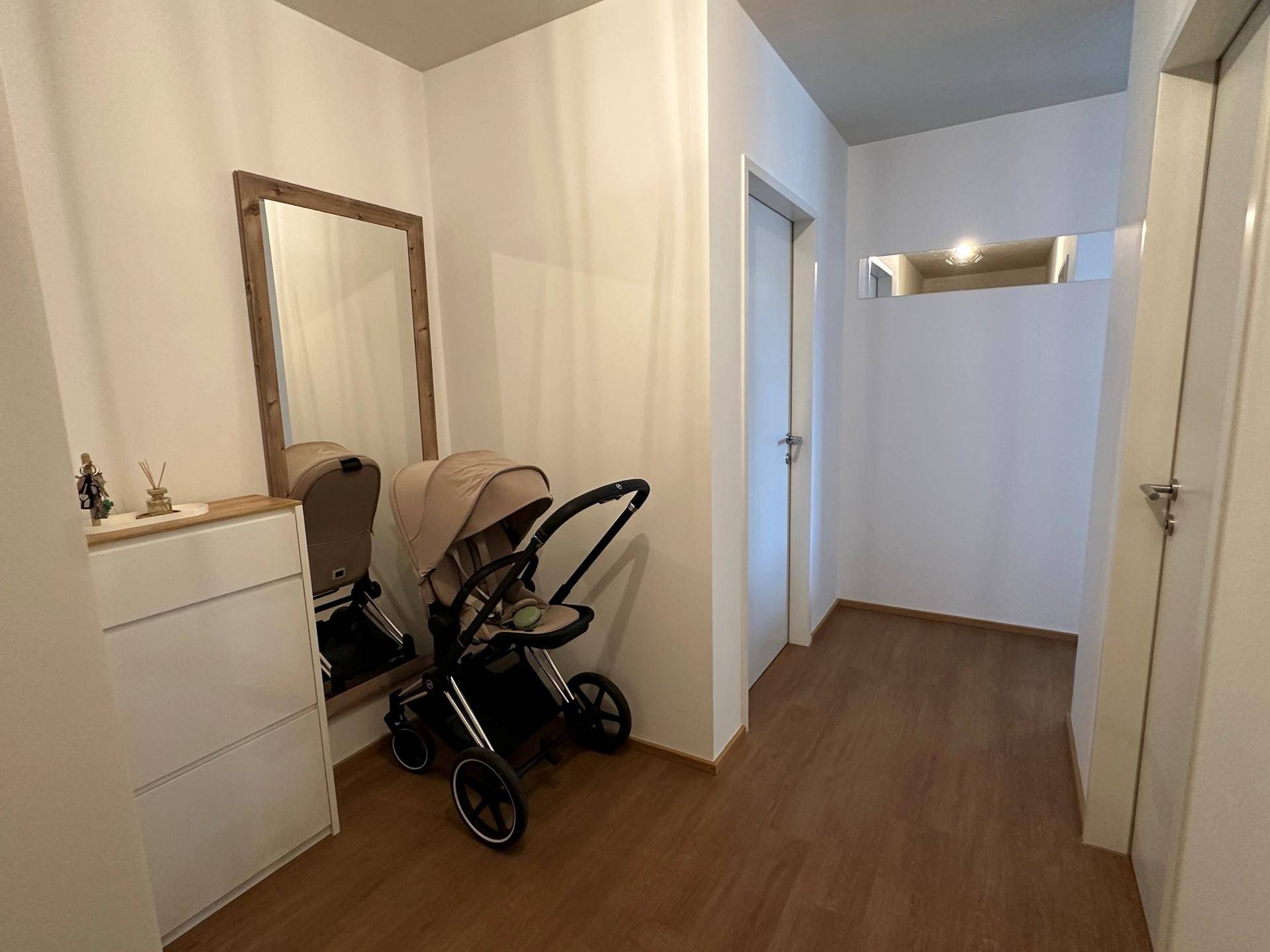 Freundlicher Flur mit großem Spiegel, Kommode und Kinderwagen, der den Eingangsbereich zeigt.