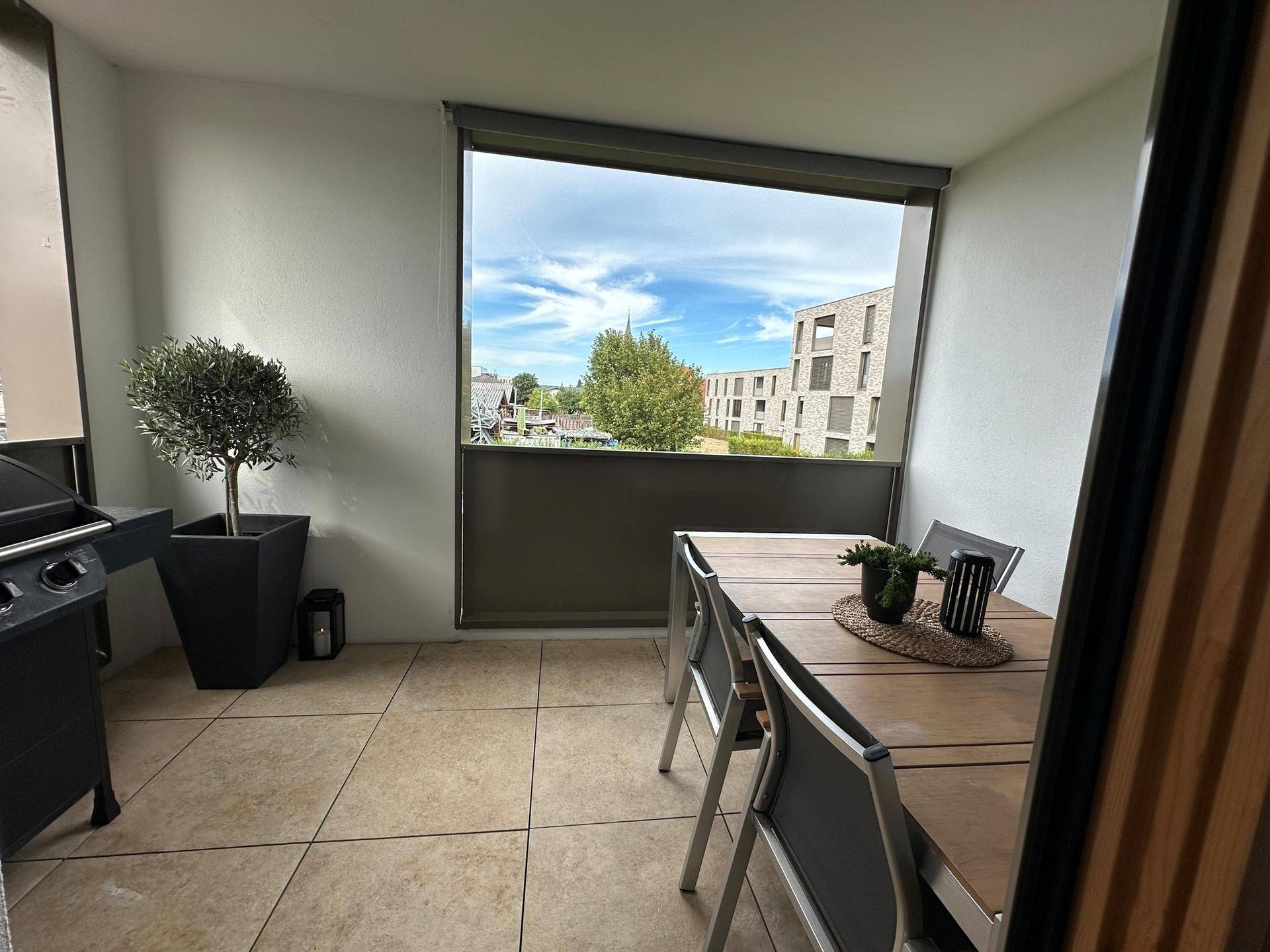 Möblierter Balkon mit Esstisch, Grill und Blick auf die umliegenden Gebäude und Grünflächen.