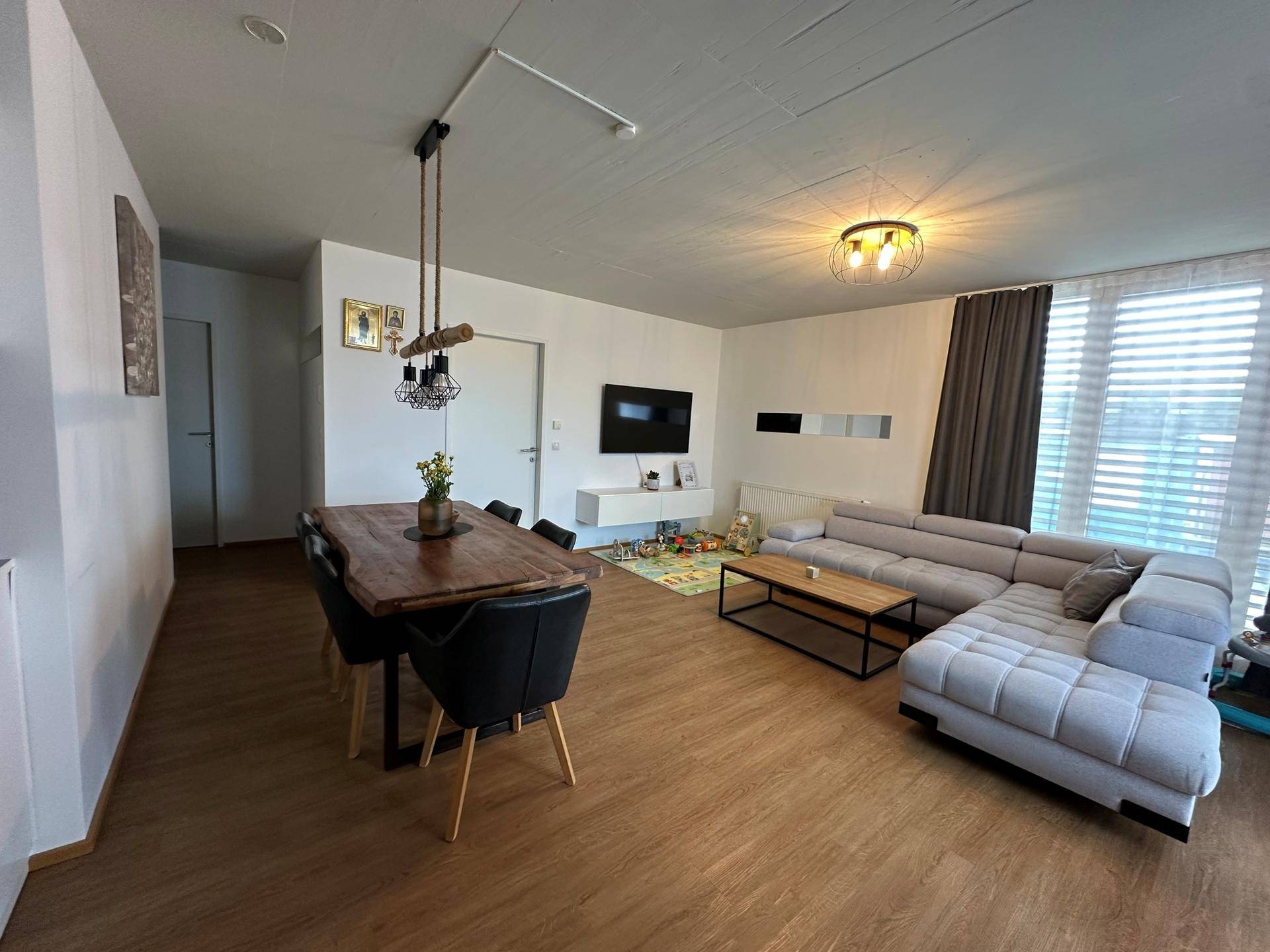 Geräumiger offener Wohn-Essbereich mit großem Ecksofa, Holztisch und Laminatboden.