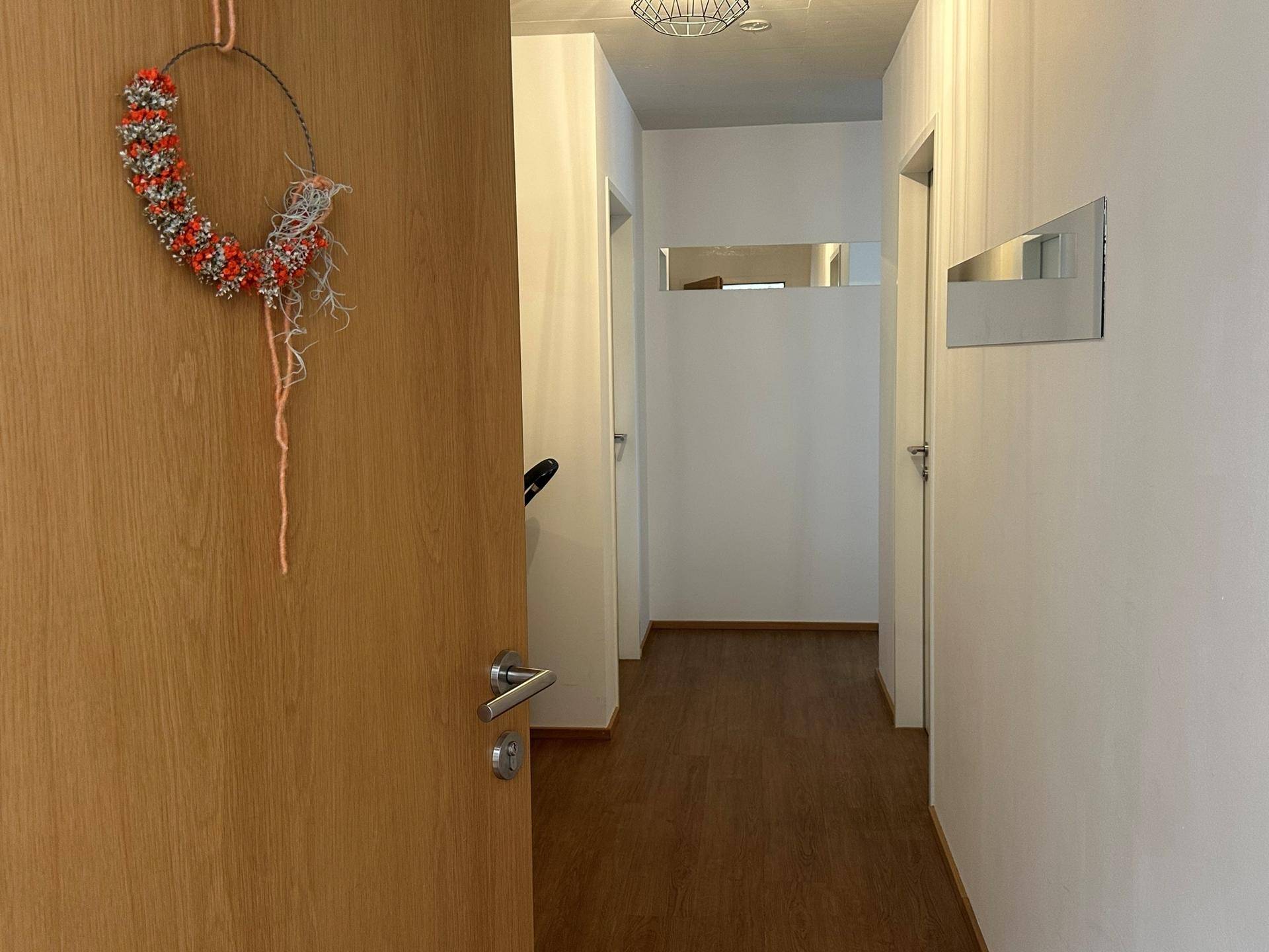 Heller Eingangsbereich mit Holztür, weiß gestrichenen Wänden und Laminatboden.