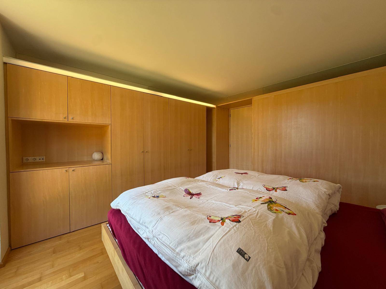 Schlafzimmer mit maßgefertigten Holz-Einbauschränken und heller Beleuchtung.