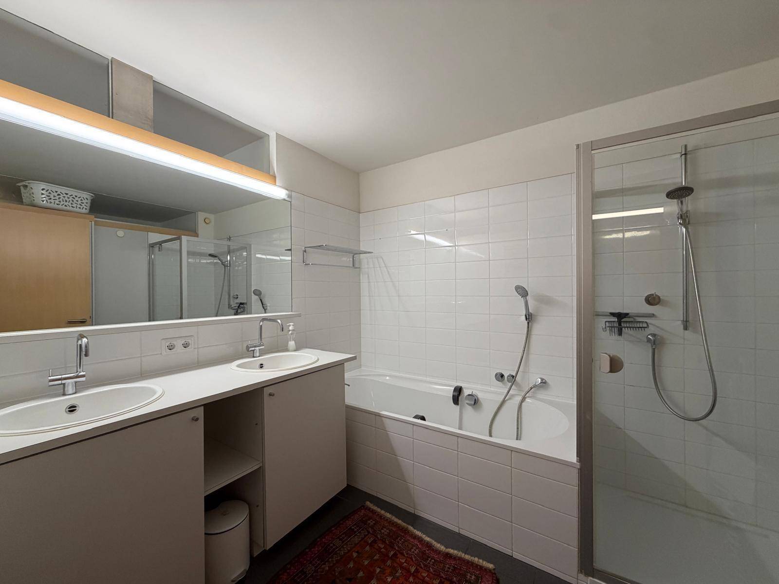Badezimmer mit Doppelwaschbecken, Badewanne und separater Duschkabine, hell gefliest.
