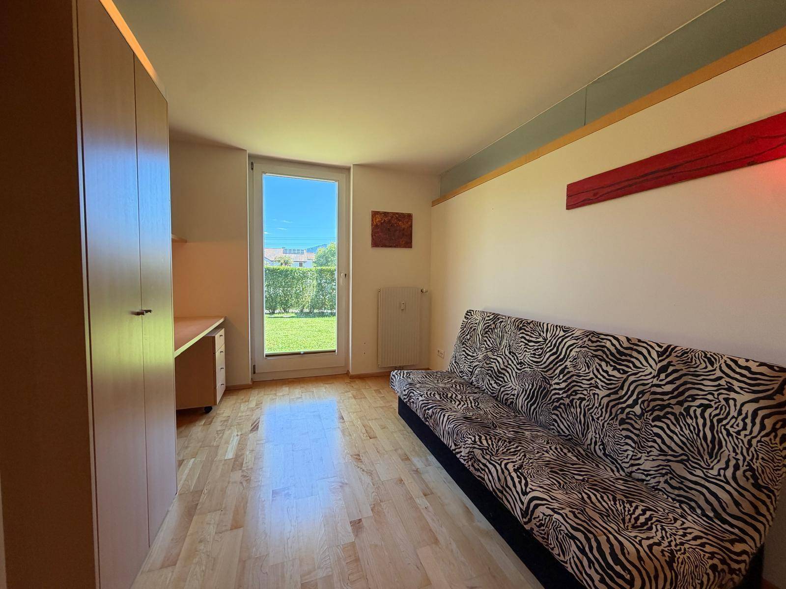 Vielseitiges Zimmer mit Schreibtisch, Schlafsofa und Zugang zum Gartenbereich.