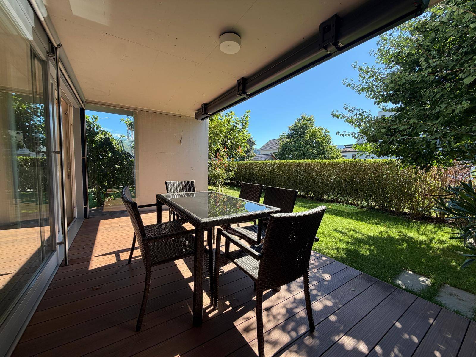 Überdachte Terrasse mit Esstisch und Stühlen, angrenzend an einen gepflegten Rasenbereich.