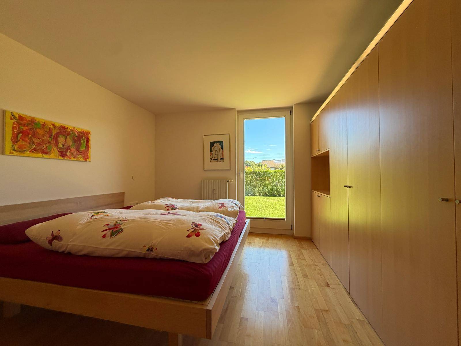 Helles Schlafzimmer mit Holzbett, Einbauschränken und direktem Zugang zum grünen Garten.