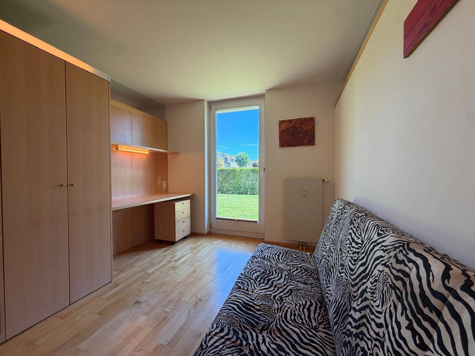 Arbeitszimmer mit integriertem Schreibtisch, Holzschrank und Blick ins Grüne.