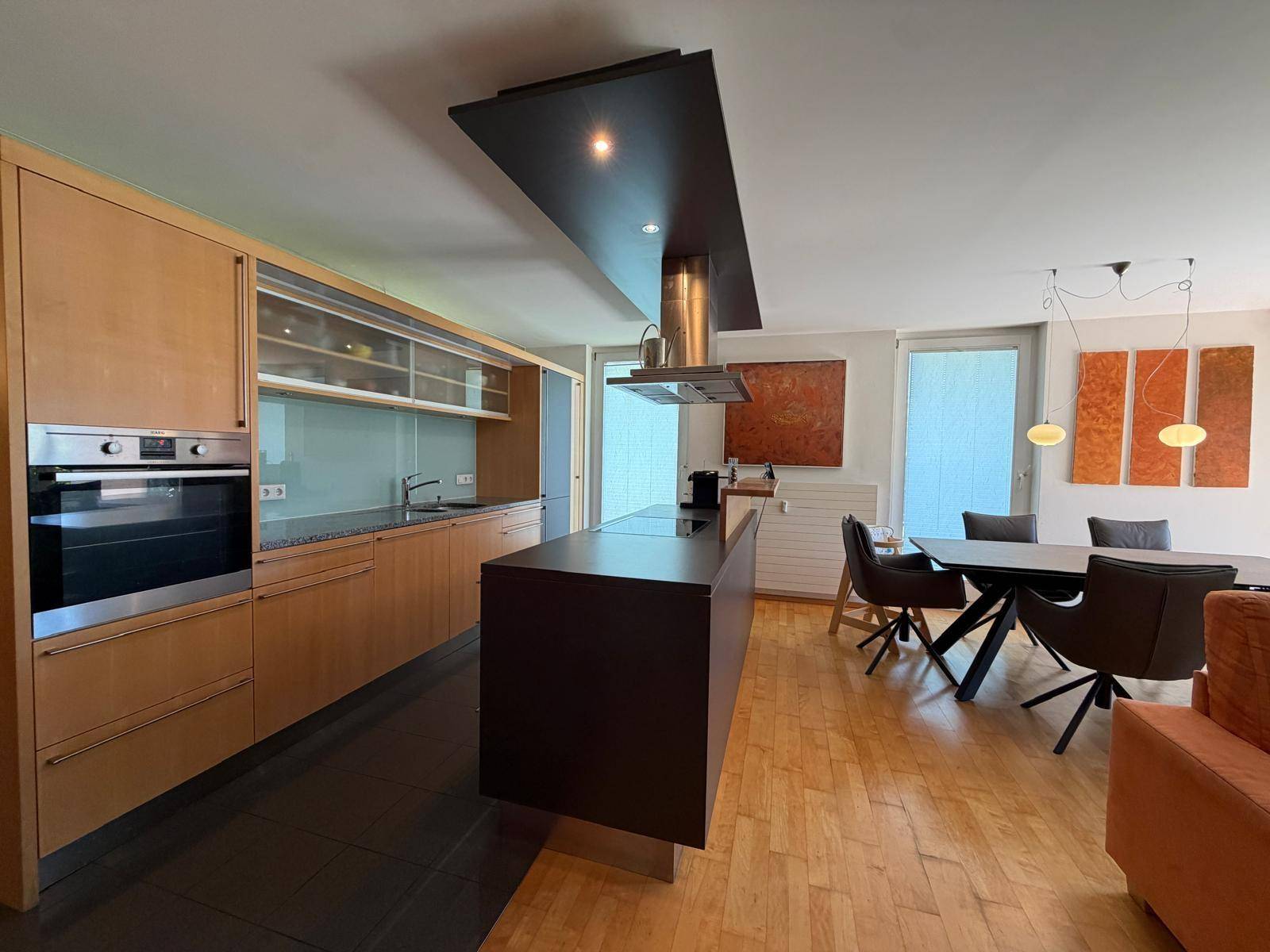 Moderne Einbauküche mit Holzfronten, Kochinsel und Essbereich in offenem Wohnkonzept.