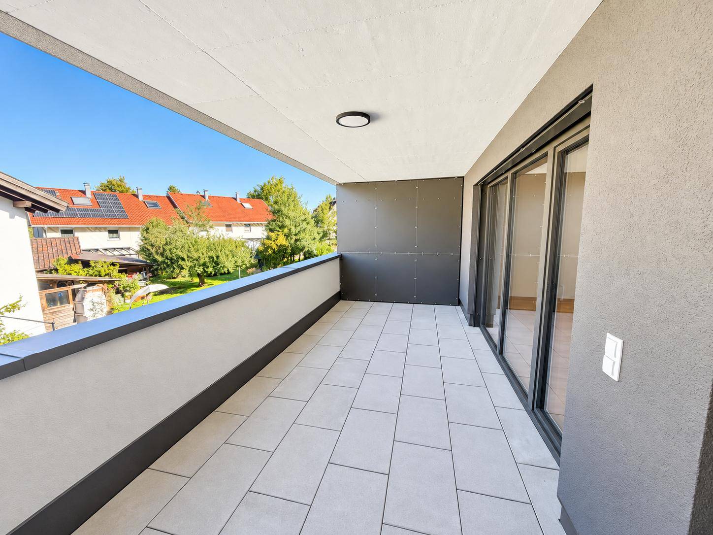 Geräumiger Balkon mit Fliesenboden und Blick auf die umliegenden Wohnhäuser und Grünflächen.