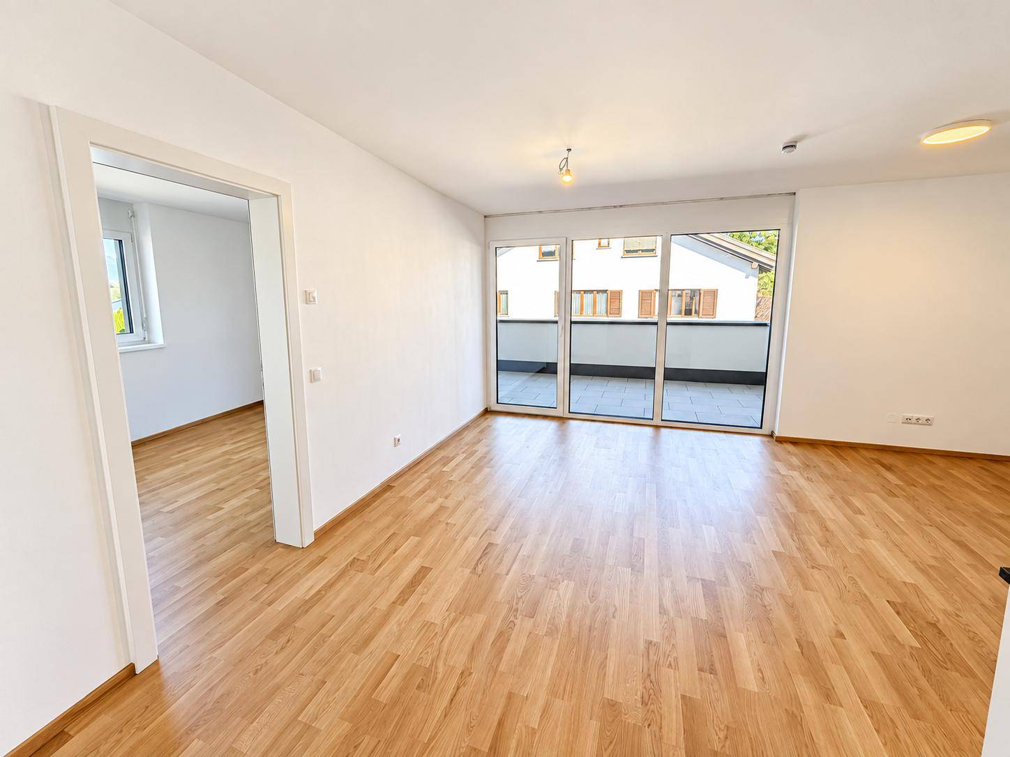 Geräumiger Wohnbereich mit Parkettboden, Zugang zu einem weiteren Zimmer und einem Balkon.