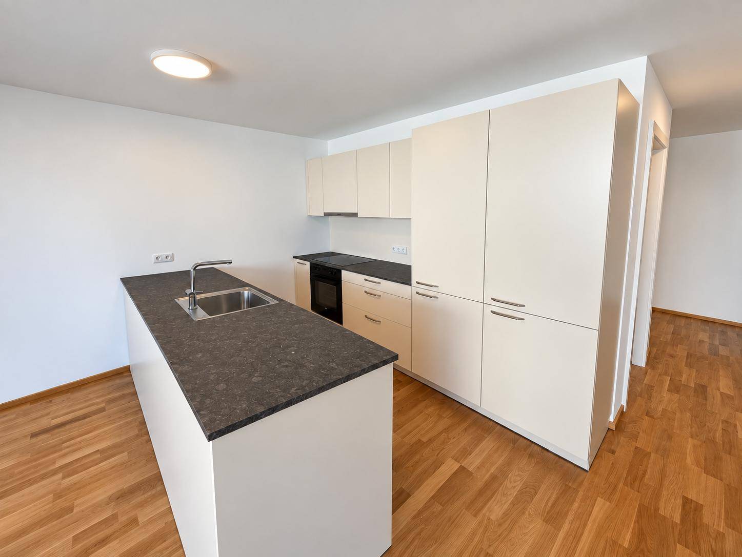 Moderne Einbauküche mit beigen Schränken, dunkler Arbeitsplatte und einer Kücheninsel mit Spüle.