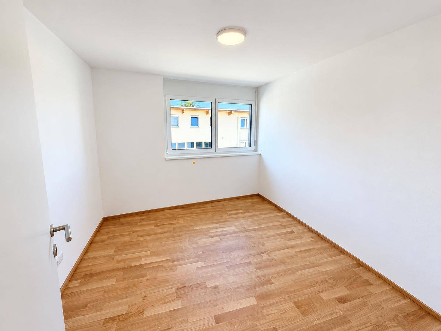 Ruhiges Zimmer mit Parkettboden und einem Fenster, das viel Tageslicht hereinlässt.