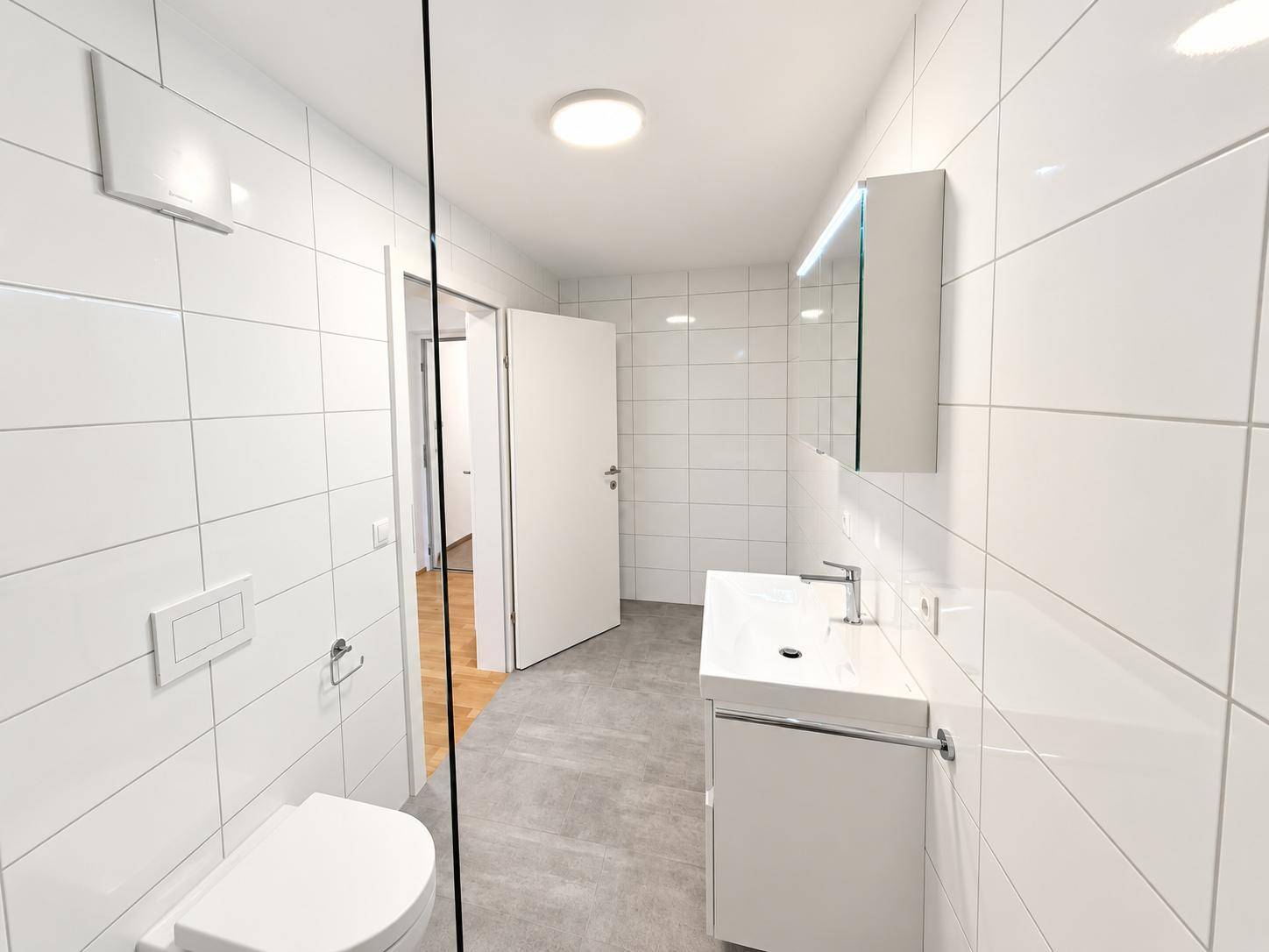 Helles Badezimmer mit modernen Fliesen, ebenerdiger Dusche und Waschtisch mit Spiegelschrank.