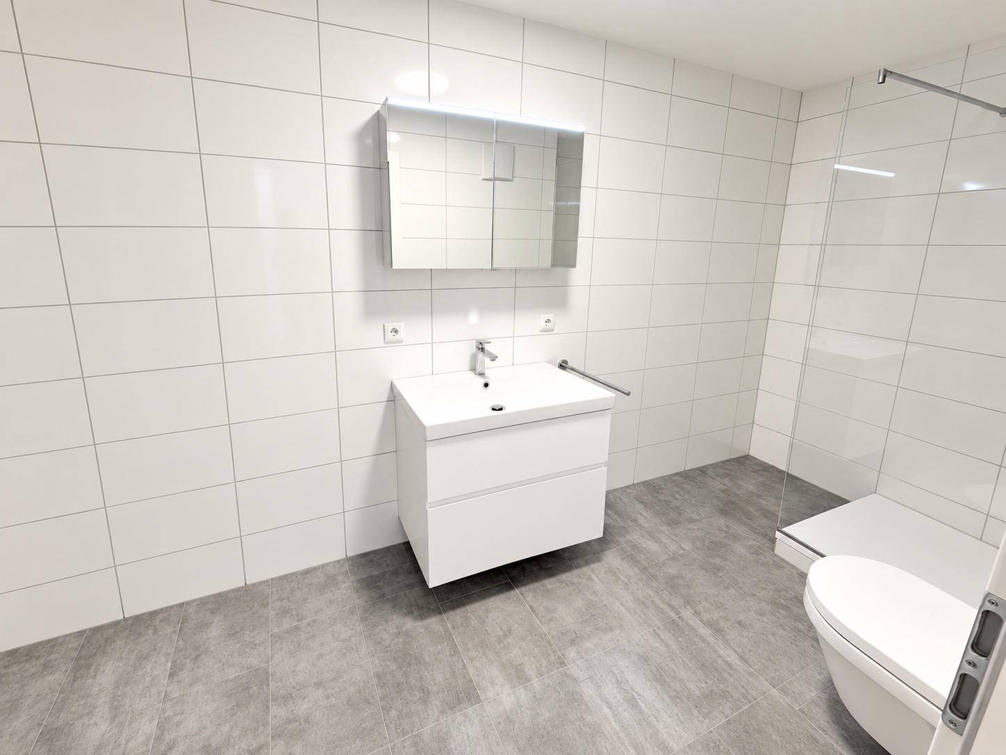 Geräumiges Badezimmer mit weißen Wandfliesen, grauen Bodenfliesen und einer modernen Dusche.