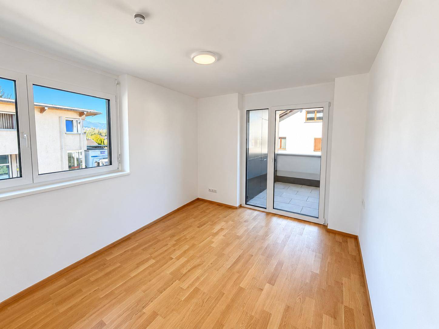 Helles Schlafzimmer mit Parkettboden, großem Fenster und direktem Zugang zum Balkon.