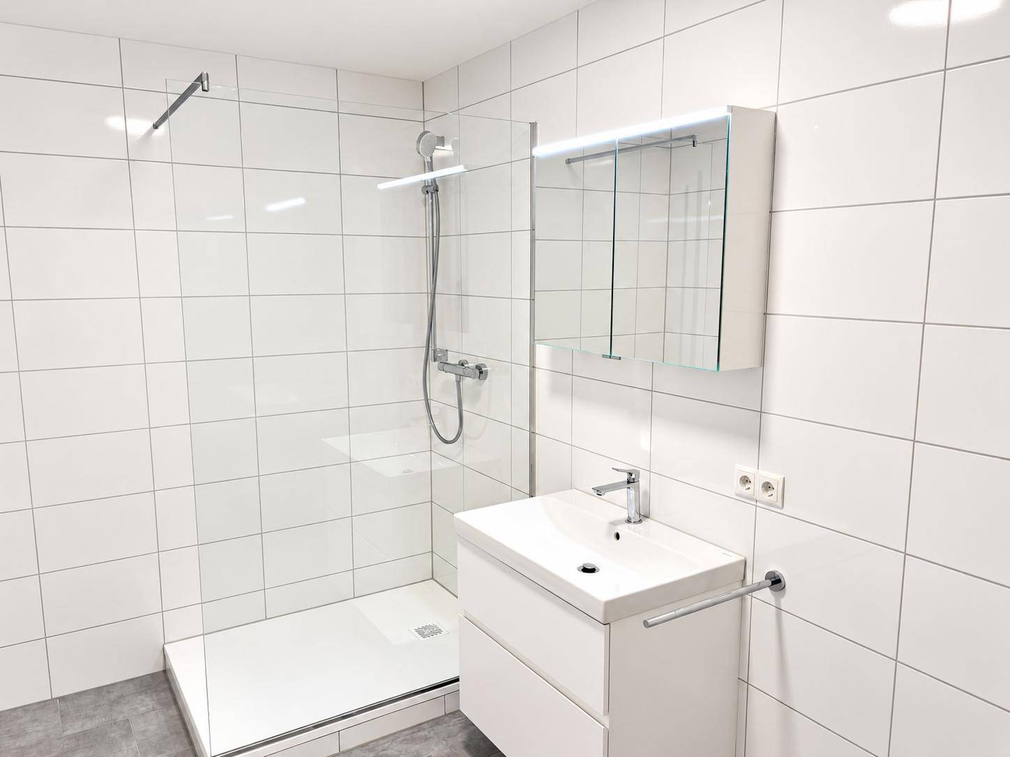 Helles Badezimmer mit ebenerdiger Dusche, modernem Waschtisch und Spiegelschrank.