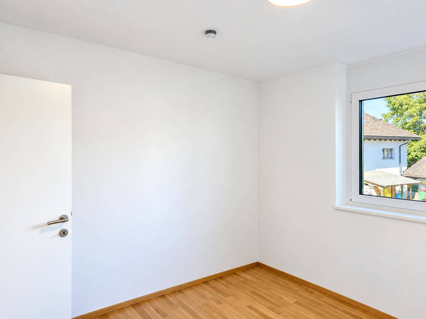 Leeres Zimmer mit Holzboden, weiß gestrichenen Wänden und einem Fenster.