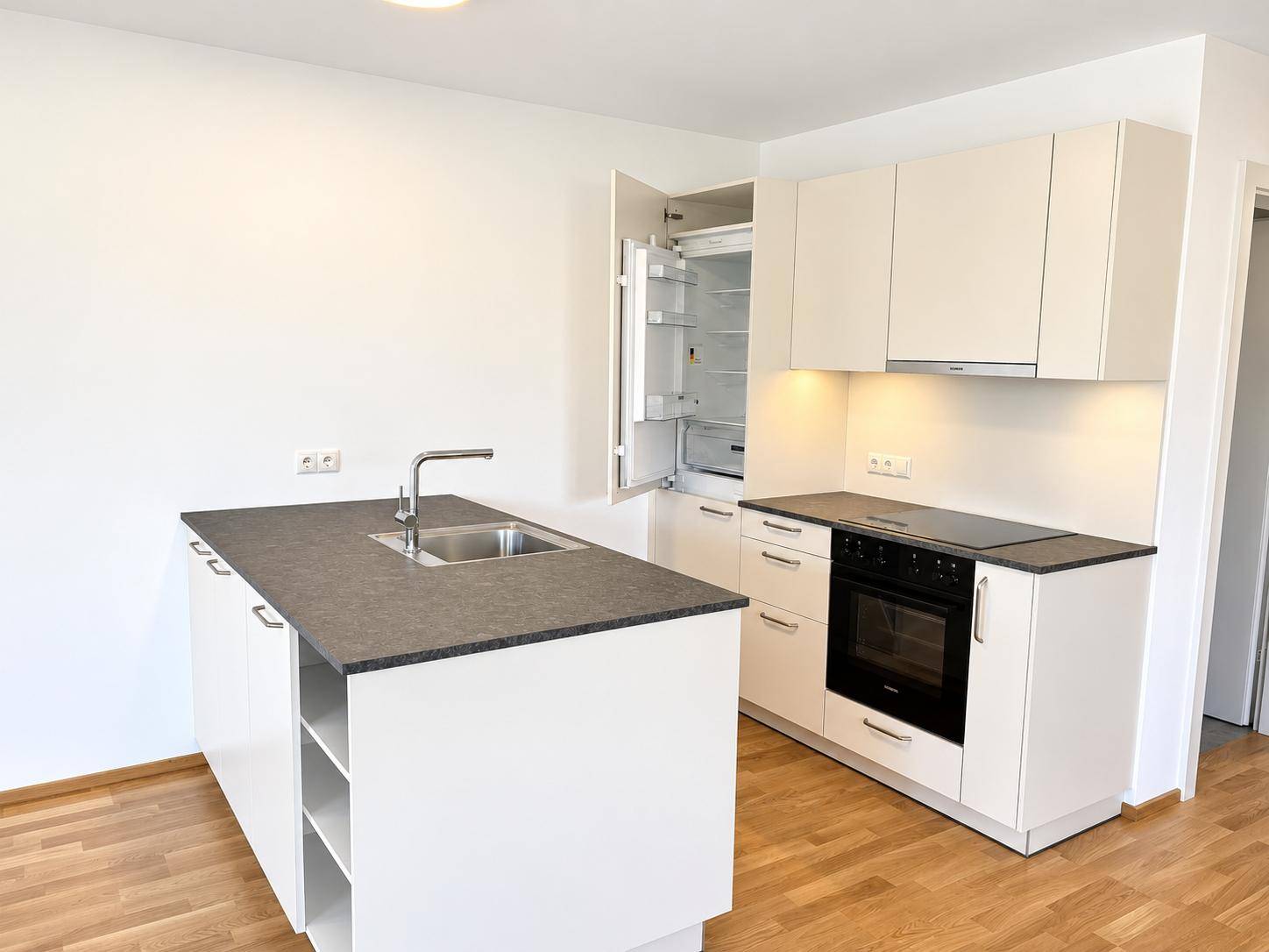 Moderne Einbauküche mit Kücheninsel, dunkler Arbeitsplatte und integrierten Geräten.