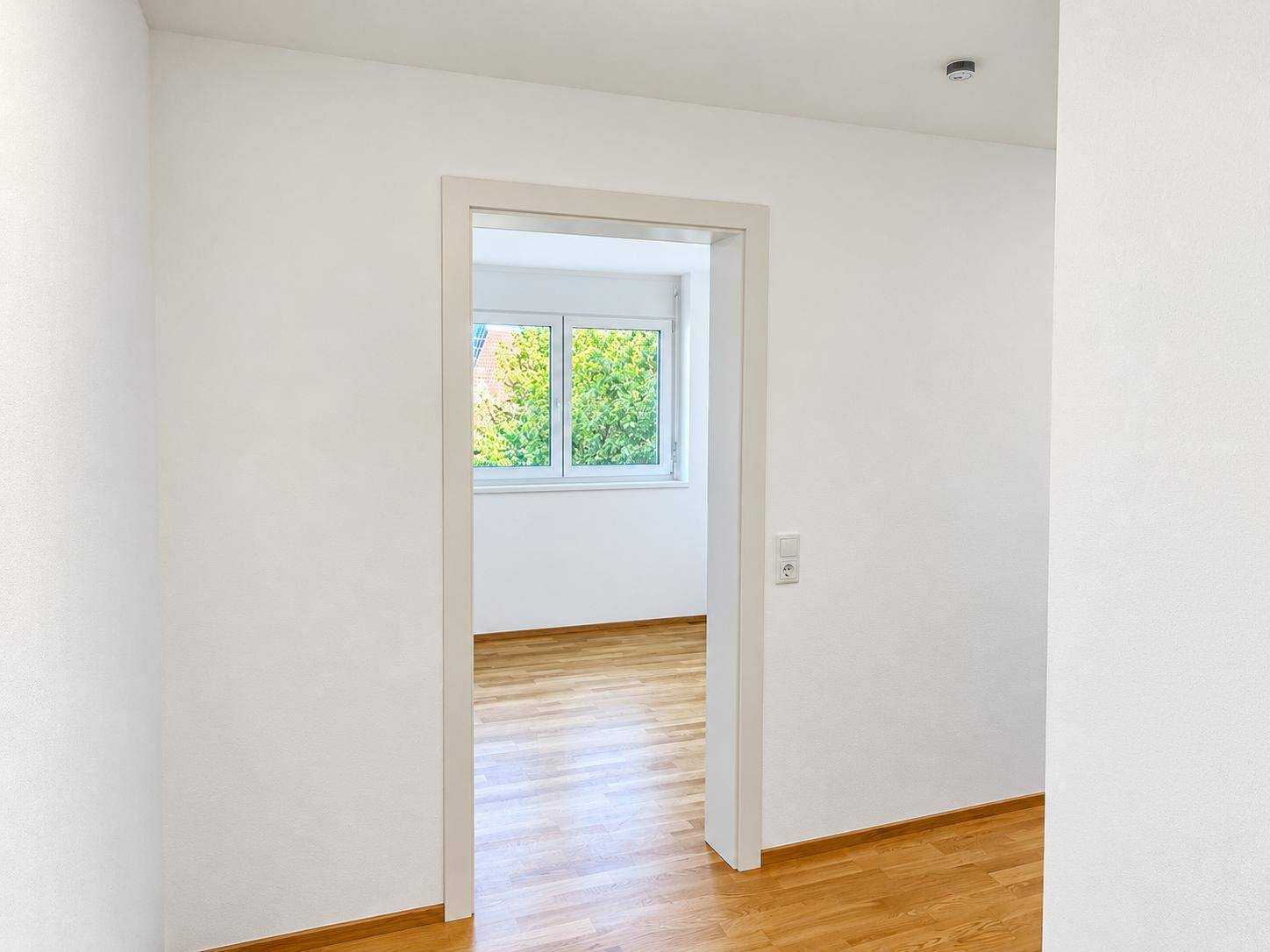 Heller Flur mit Holzboden, der in ein weiteres Zimmer mit Fenster führt.