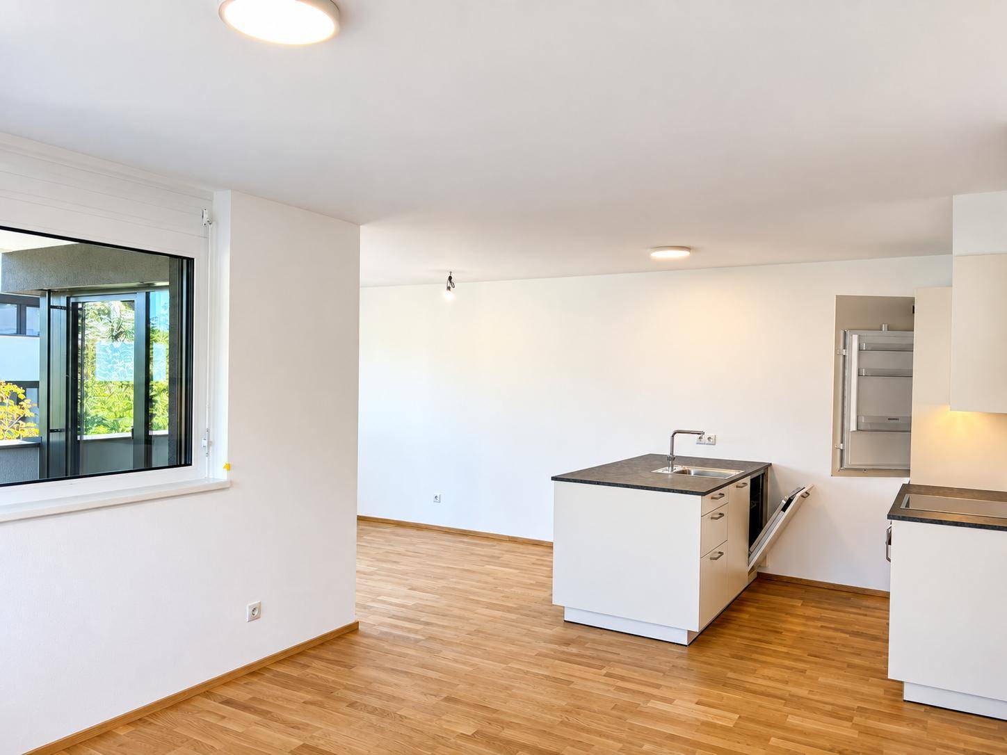 Offener Wohnbereich mit Kücheninsel, Holzboden und großem Fenster.