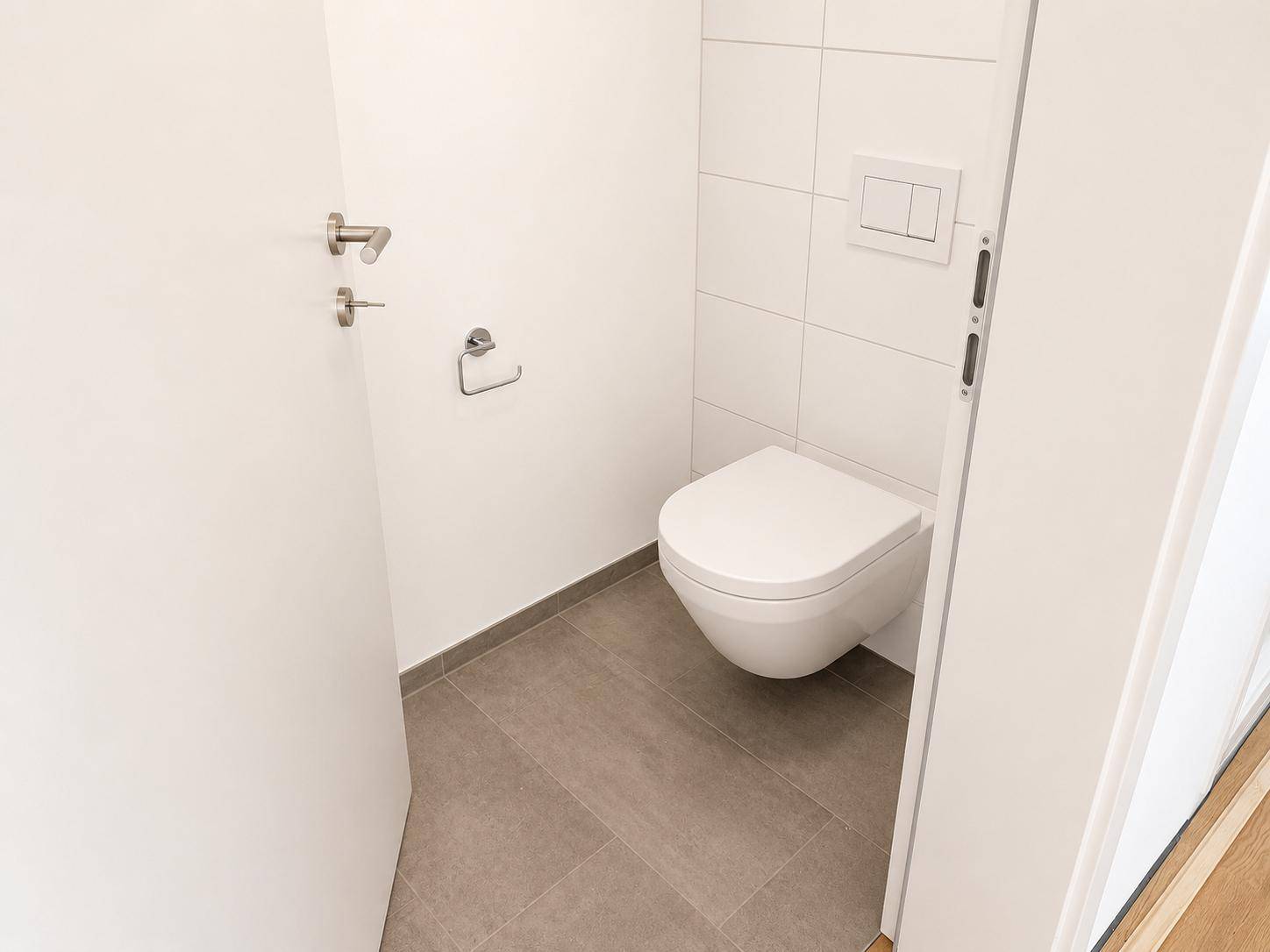 Separates Gäste-WC mit wandhängender Toilette und modernen weißen Fliesen.