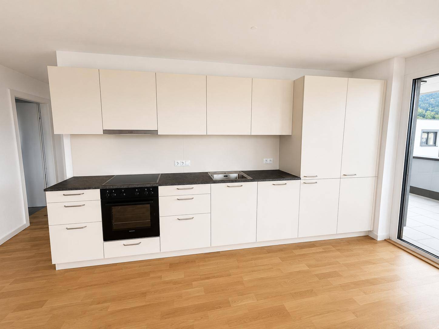 Moderne, unbenutzte Küche mit weißen Schränken, dunkler Arbeitsplatte und integrierten Geräten.