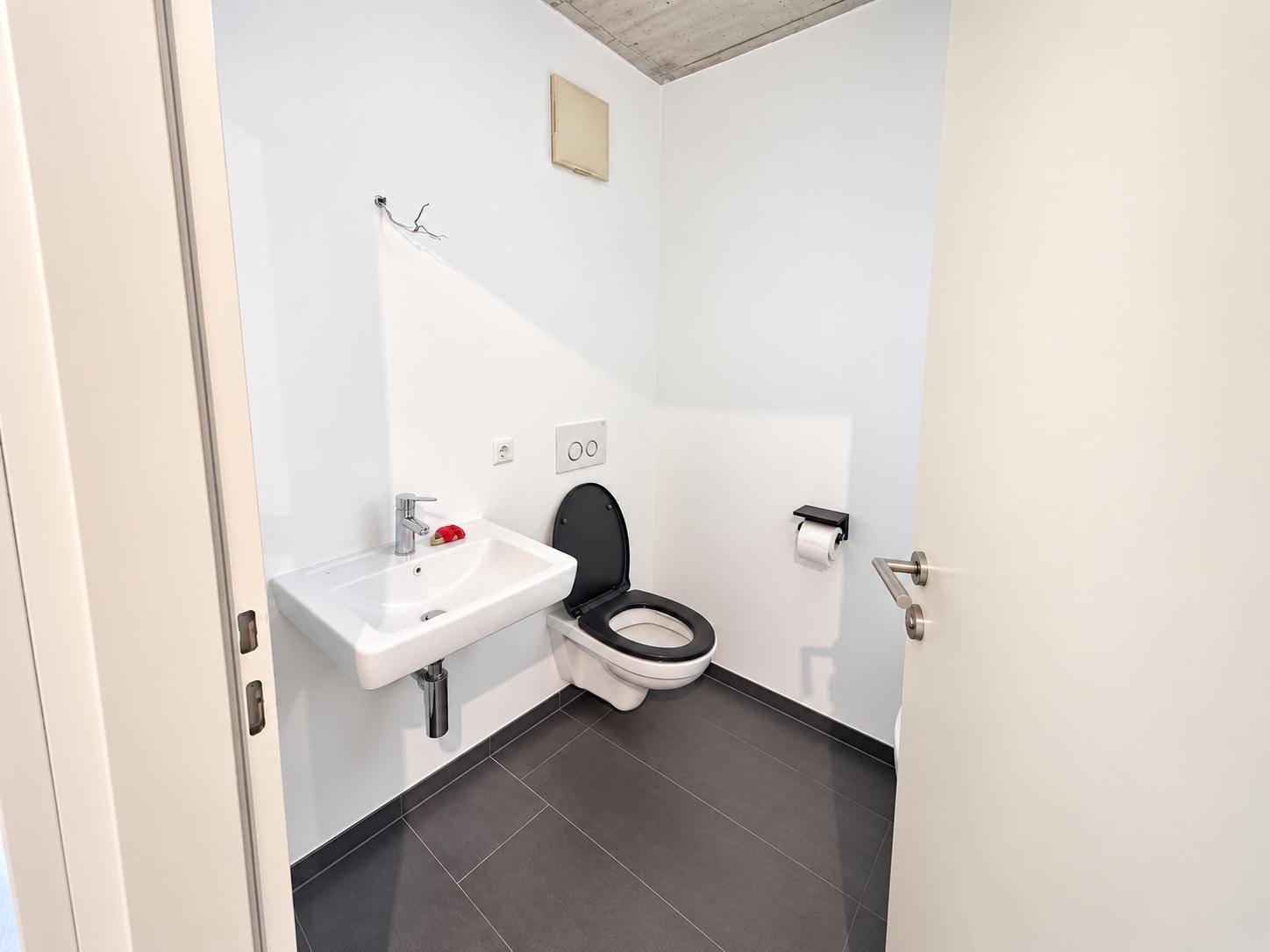 Separates Gäste-WC mit Wand-WC, Waschbecken und dunklen Bodenfliesen.