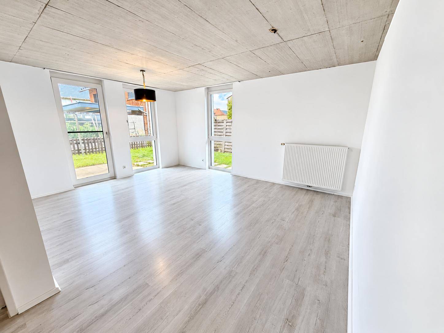 Geräumiges Wohnzimmer mit hellem Laminatboden, Sichtbetondecke und Zugang zum Garten.