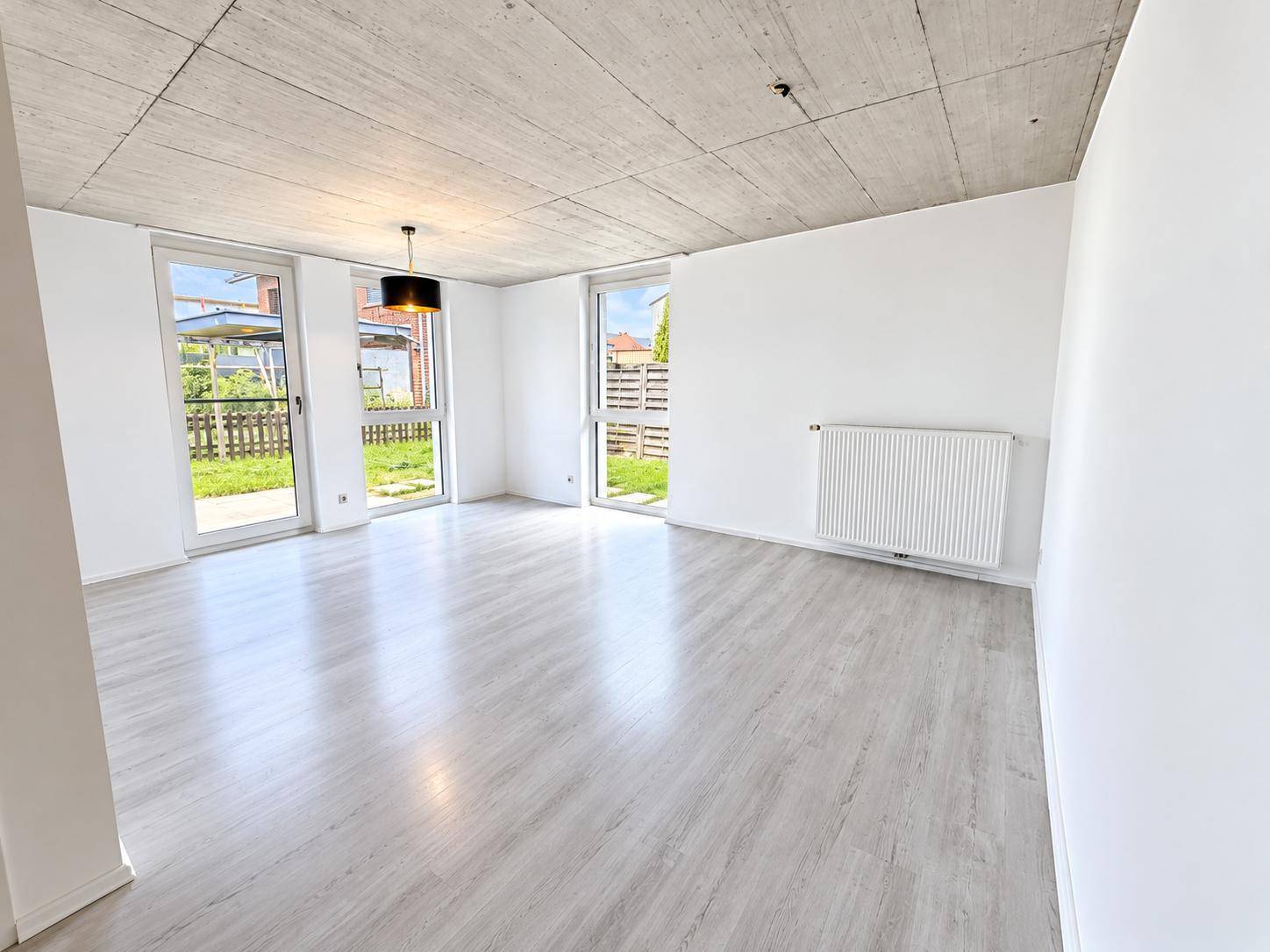 Geräumiges Wohnzimmer mit hellem Laminatboden, Sichtbetondecke und Zugang zum Garten.