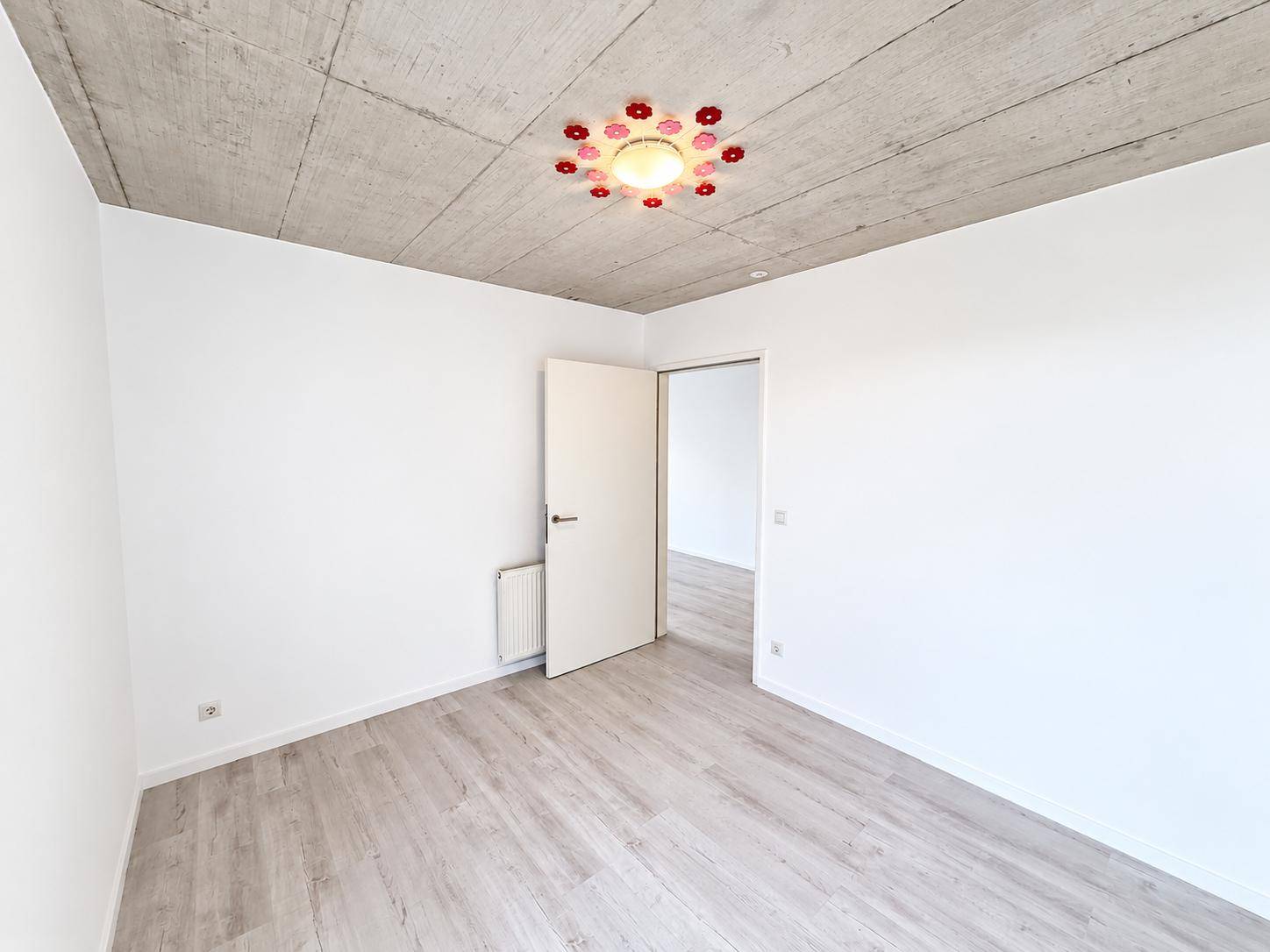 Schlafzimmer mit hellem Laminatboden, Sichtbetondecke und einer modernen Deckenleuchte.