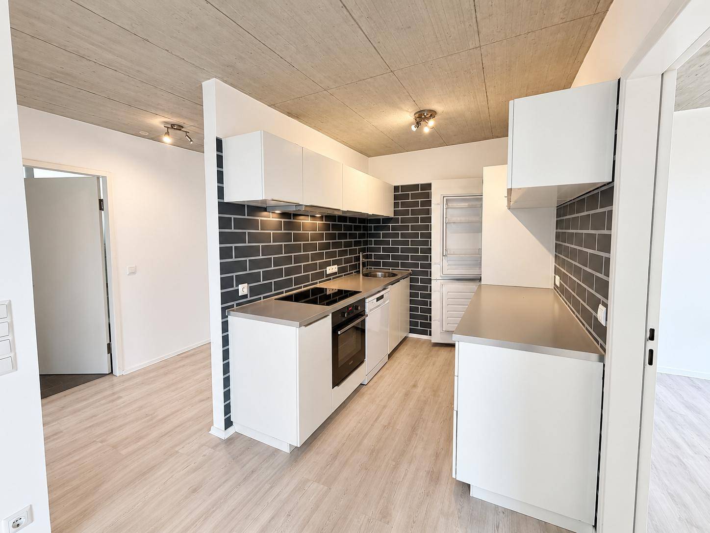 Moderne Einbauküche mit weißen Schränken, integrierten Geräten und dunklem Fliesenspiegel.