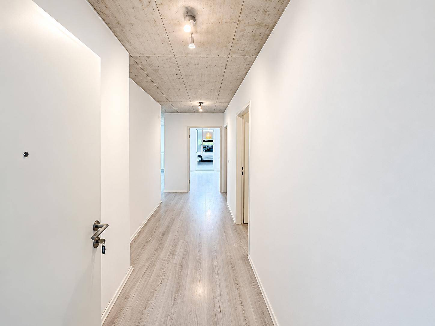 Heller Flur mit modernem Laminatboden und Sichtbetondecke, der zu weiteren Räumen führt.