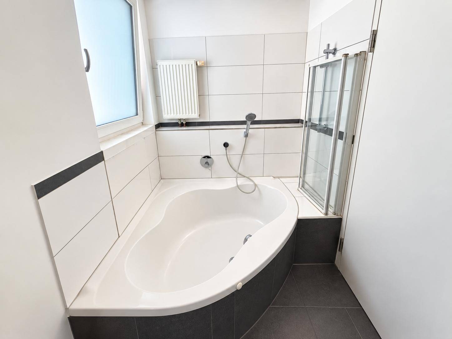 Modernes Badezimmer mit Badewanne, Duschabtrennung und Fenster für Tageslicht.
