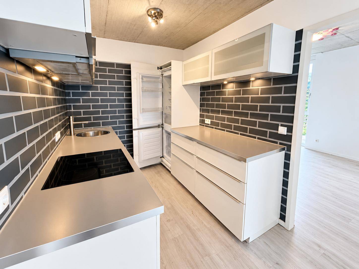 Moderne Küche mit weißen Schränken, Edelstahl-Arbeitsplatten und dunklem Fliesenspiegel.