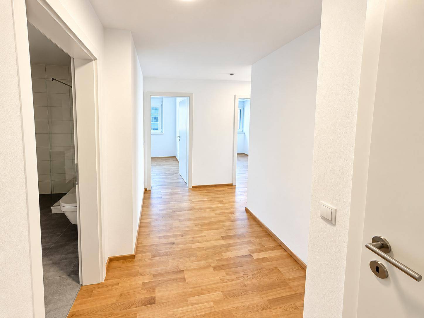 Heller Flur mit Holzparkettboden und Zugang zu verschiedenen Zimmern und einem Badezimmer.