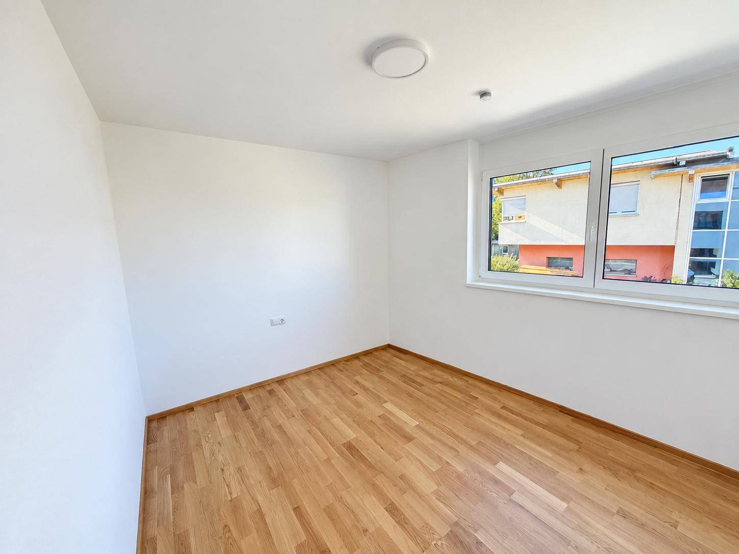 Helles Zimmer mit Holzparkettboden und einem Fenster, das eine angenehme Wohnatmosphäre schafft.