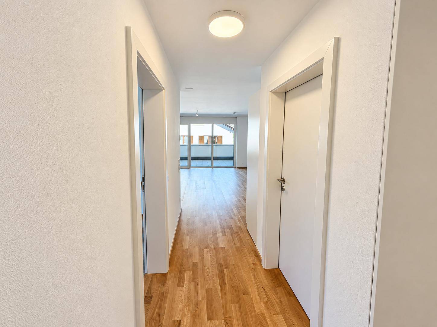Langer, heller Flur mit Holzparkettboden, der den Blick auf einen offenen Wohnbereich freigibt.