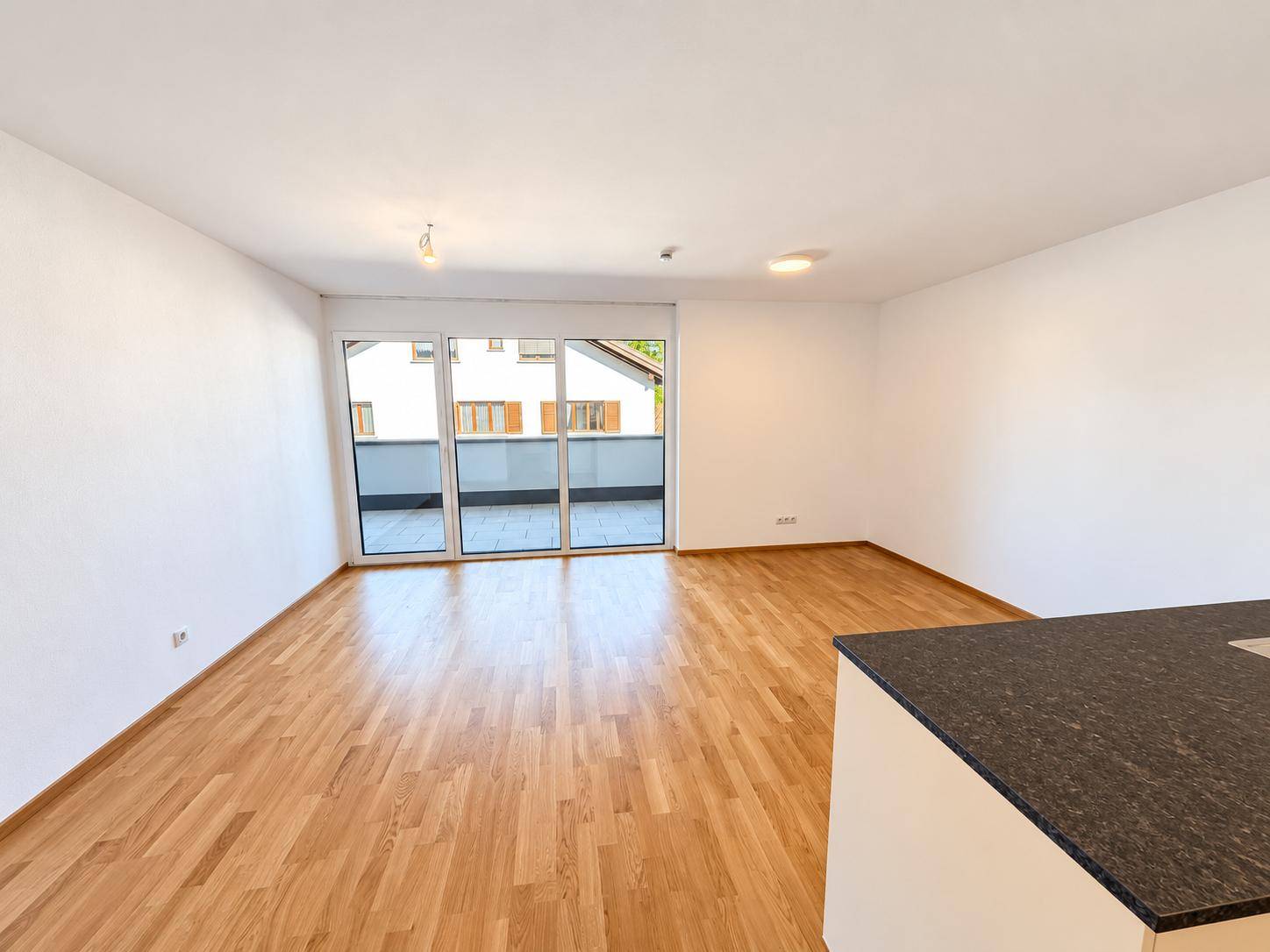 Heller Wohnbereich mit Holzparkettboden und großzügigem Zugang zu einem Außenbalkon.