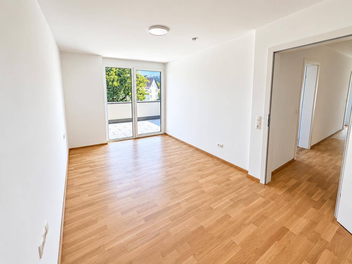 Geräumiges Wohnzimmer mit Holzparkettboden, großen Fenstern und Zugang zum Balkon.
