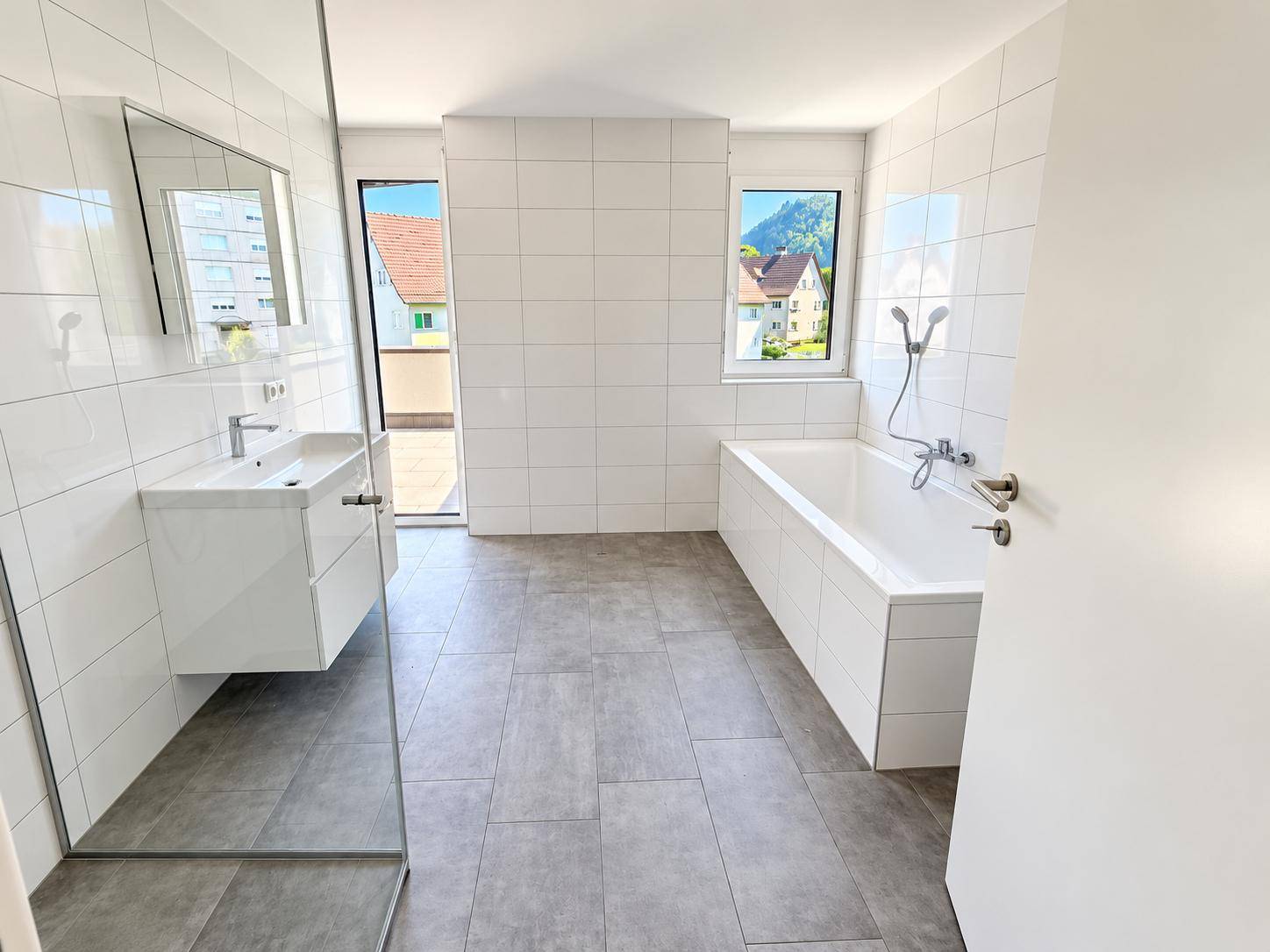 Modernes Badezimmer mit Badewanne, Dusche, Waschbecken und Zugang zur Terrasse.