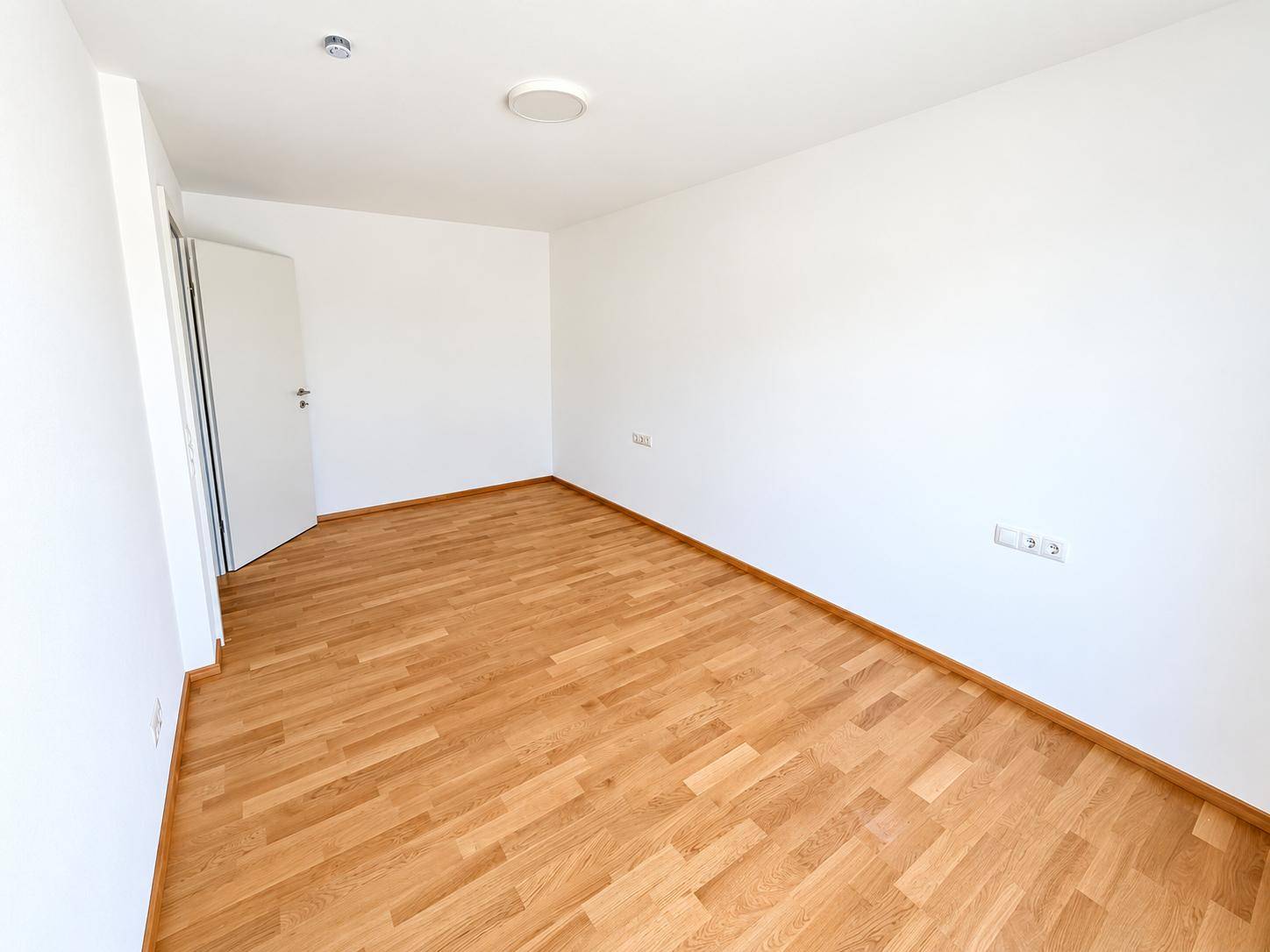Leerer Raum mit Holzparkettboden und weißen Wänden, bereit zur individuellen Gestaltung.