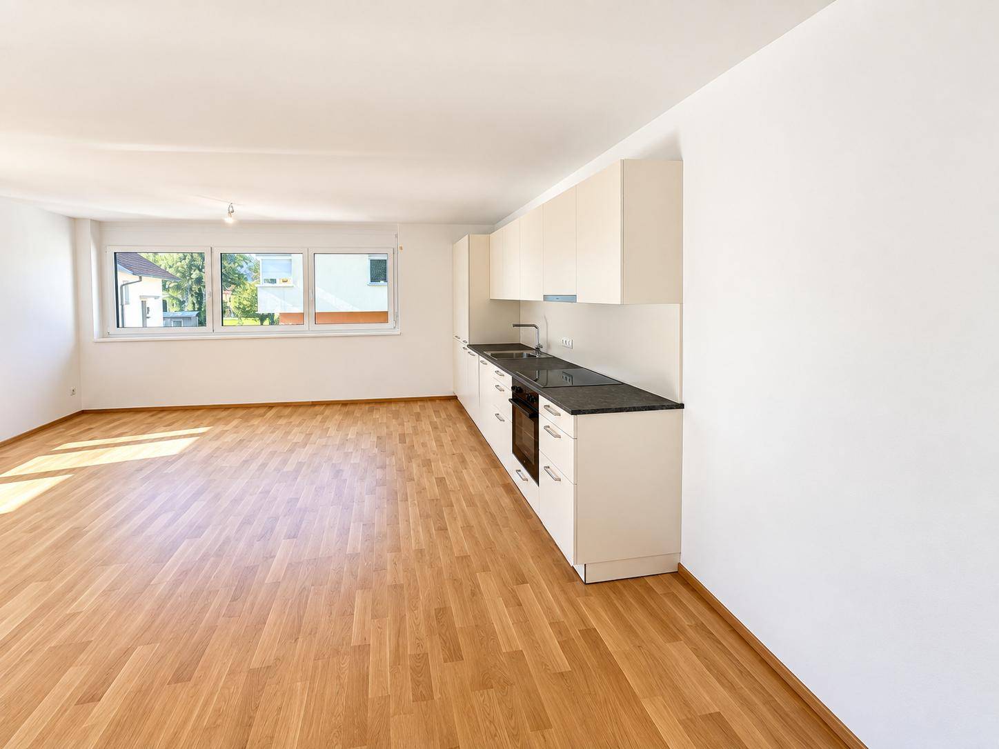 Moderne Einbauküche mit weißen Schränken, dunkler Arbeitsplatte und integriertem Backofen.
