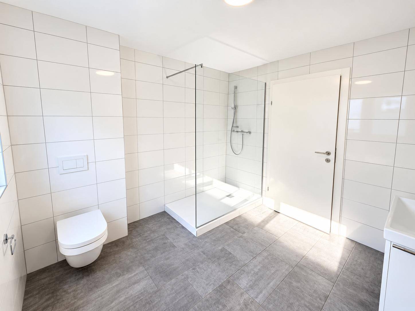 Modernes Badezimmer mit weißen Fliesen, ebenerdiger Dusche und wandhängendem WC.