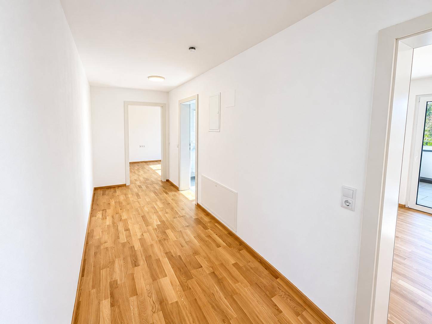 Heller Flur mit modernem Holzparkett und weißen Wänden, der zu weiteren Räumen führt.