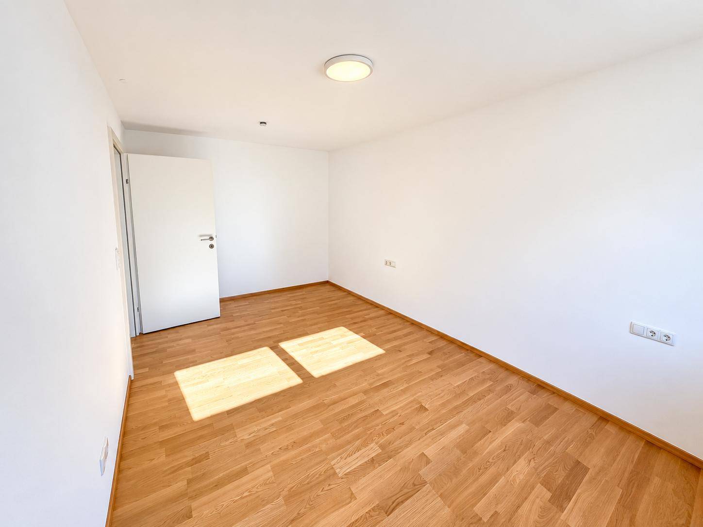 Leeres Zimmer mit hellem Holzboden und weißen Wänden, ideal als Schlaf- oder Arbeitszimmer.