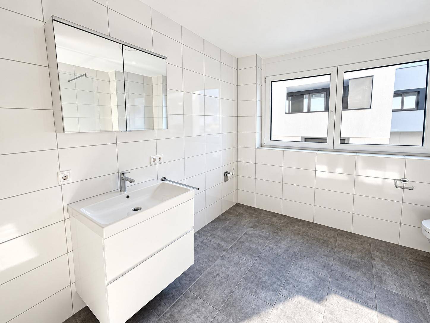 Helles Badezimmer mit Fenster, modernem Waschtisch und Spiegelschrank.