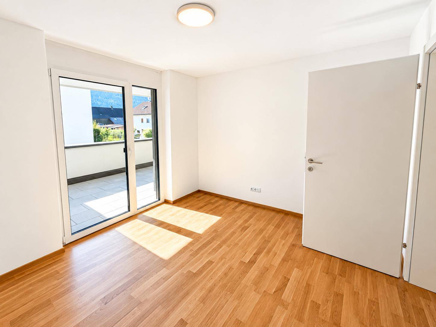 Helles Schlafzimmer mit Holzboden und direktem Zugang zu einem sonnigen Balkon.