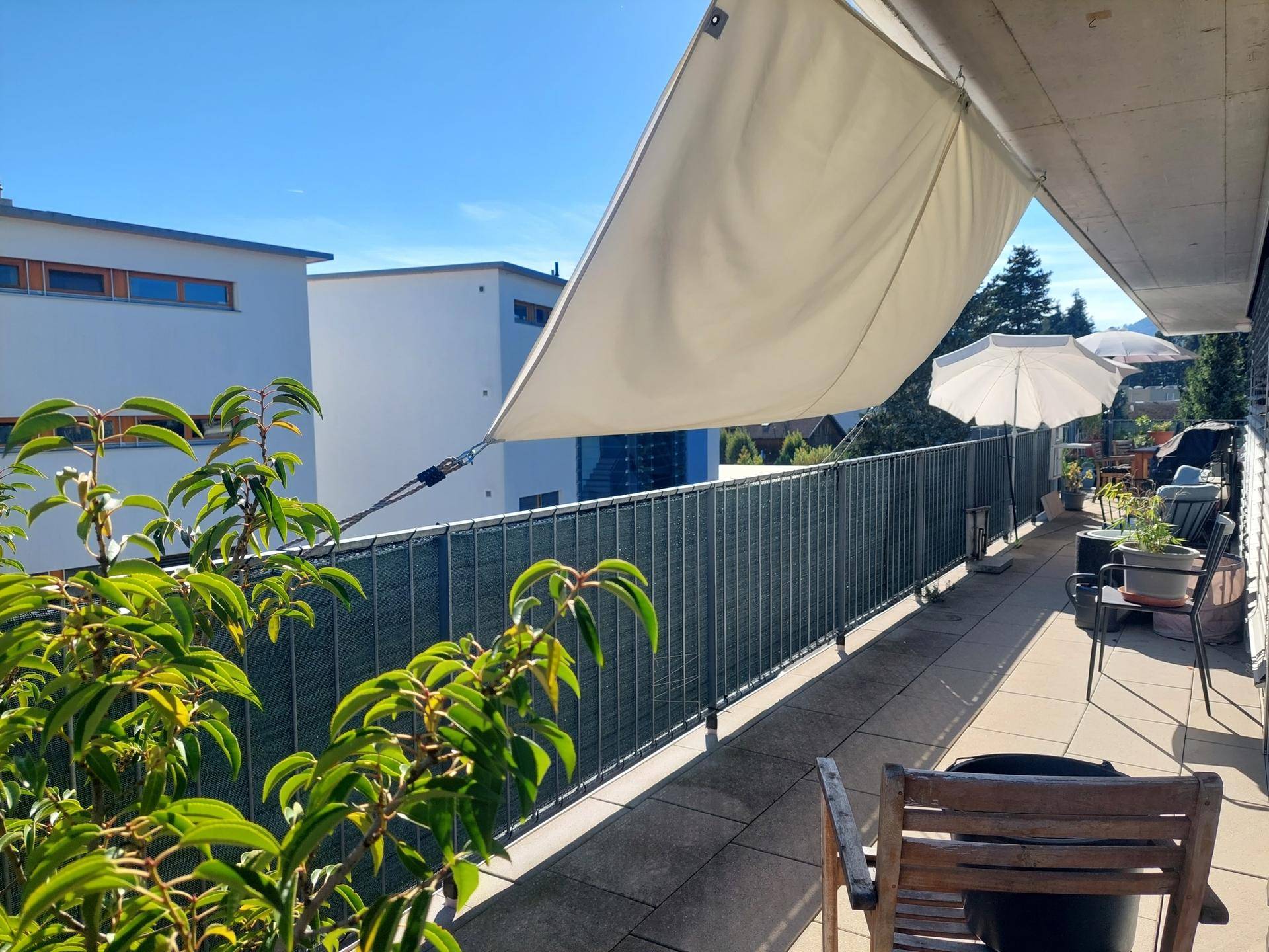Geräumiger Balkon mit Sonnensegel, Pflanzen und Gartenmöbeln, ideal für entspannte Stunden im Freien.